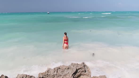 Young Woman in a Red Swimsuit Walks Into the Turquoise Ocean on a Paradise Beach