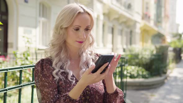 A Middleaged Caucasian Woman Works on a Smartphone and Smiles at the Camera in an Urban Area