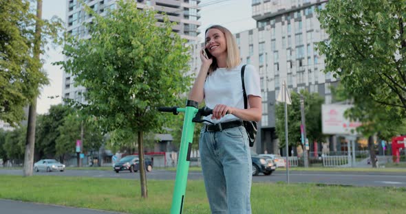 Beautiful woman standing next to electric scooter while using her phone.