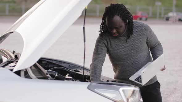 Young African American Black Man Repairing the Car While Using Laptop