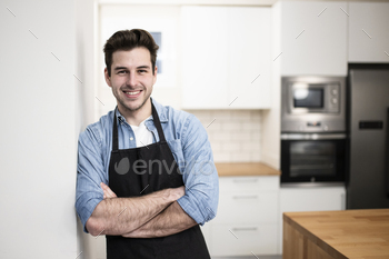 handsome young man smiling in the kitchen wearing an apron - Portrait of a cheerful confident