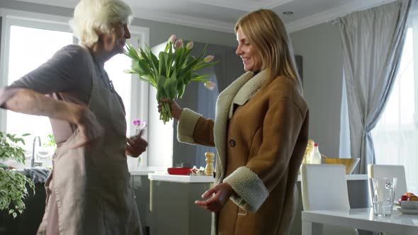 Young Woman Visiting Mother and Giving her Flowers at Holiday
