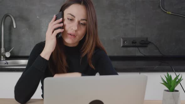 Attractive Woman Talking on Cellphone While Working on Laptop at Home