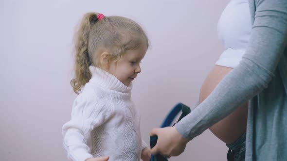 Girl Puts Headphones on Waist with Pregnant Mother at Wall