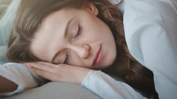 Young Woman with Long Hair Wakes Up, Gets Up on Bed and Stretches in Morning Sun Light