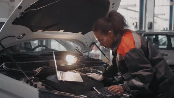 Female Auto Mechanic Using Laptop and Tool to Fix Car