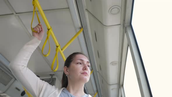 Pretty Woman Stands in Tram Holding Handrail Travelling to City