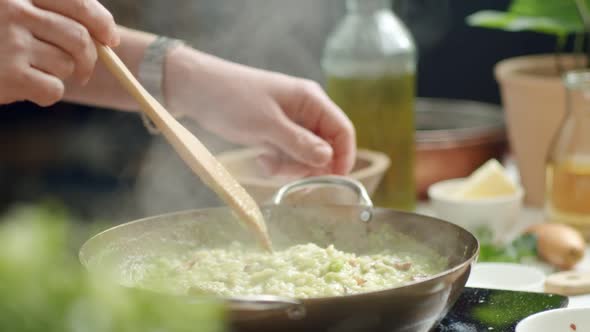 Crop chef stirring hot risotto in pan