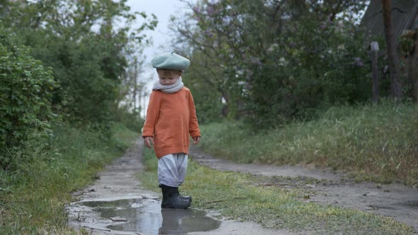 Happy Childhood, an Attractive Male Kid in a Hat and Rubber Boots, Having Fun Playing Outdoors