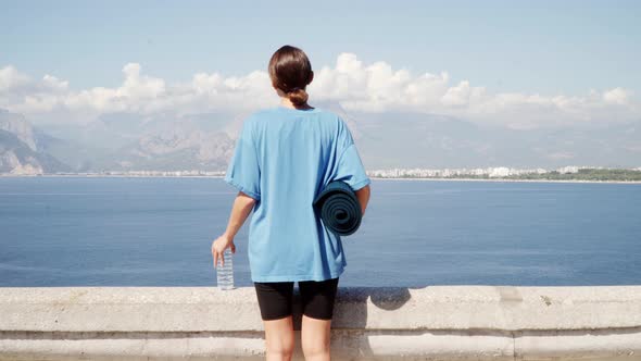 Girl with a Yoga Mat and Water on the Background of the Sea