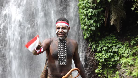 Papua man of Dani tribe saying Merdeka, celebrating Indonesia independence day against waterfall bac