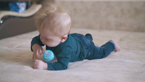 Funny Boy Crawls with Bottle on Large Beige Bed in Room