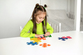 Girl sitting at desk in children's room, putting colored puzzle pieces together - PhotoDune Item for Sale