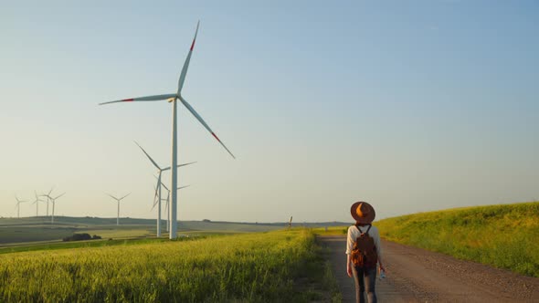 Attractive woman with a backpack in a field with eco windmills