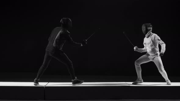 Two Men in Helmets and Uniform Fencing Over Dark Background