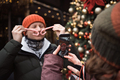 child free couple wearing hats and winter clothes taking pictures by phone at christmas city market - PhotoDune Item for Sale