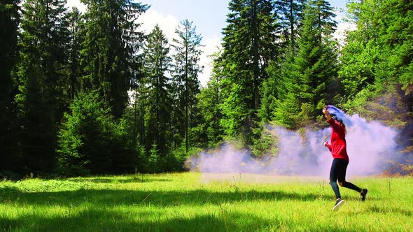 SLOWMO, Woman in red sweatshirt with blue smoke bomb runs and skips around a forest meadow. Black Fo