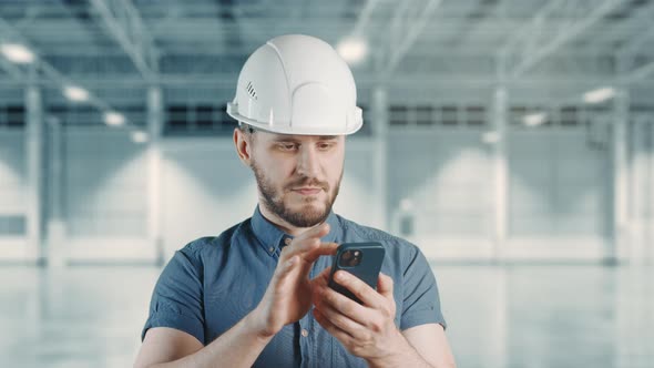 A Man Construction Worker with Helmet is Using Mobile Phone at Building Site