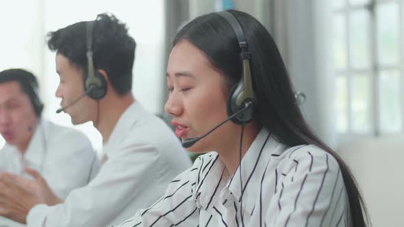 A Woman Of Three Asian Call Centre Agents Speaking To Customer While Her Colleagues Are Talking