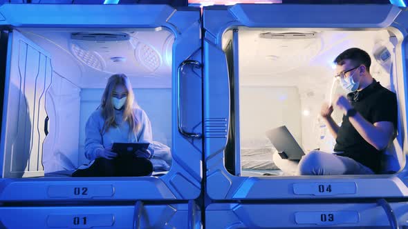 Adjoined Rooms of a Capsule Hotel with Young People in Face Masks