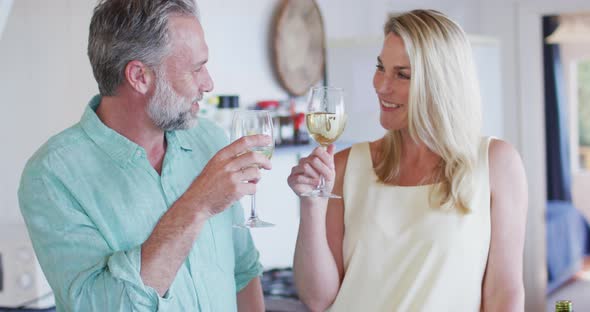 Happy caucasian mature couple cooking together and drinking wine in the kitchen