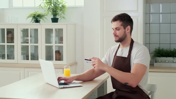 A Man Pays for Online Delivery of Food to His Home Using a Credit Card While Sitting in the Kitchen