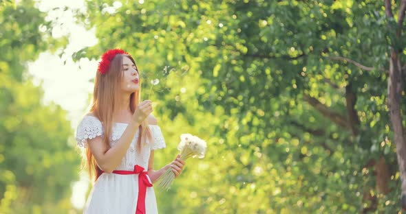 Young Beautiful Woman Walks in the Forest and Blows on White Dandelions Flower Flies