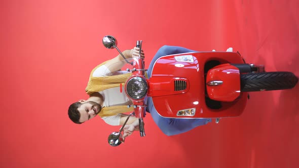 Portrait of a Serious Man Sitting on a Scooter in Isolation on a Red Studio Background, a Young Man