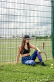 A tired woman is sitting on the grass by the tennis court with a bottle of water - PhotoDune Item for Sale
