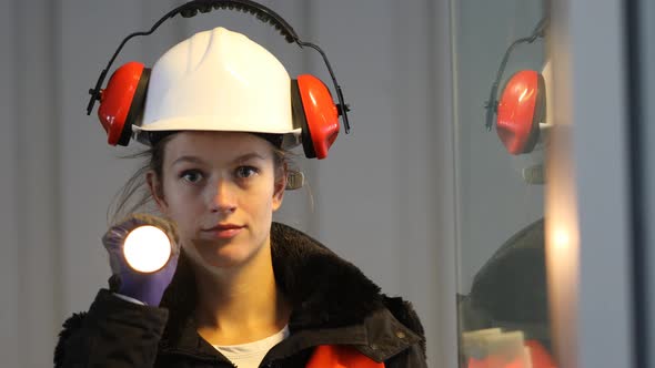 Smiling female worker with torch, helmet and ear muffs