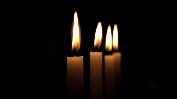 Flames of four candles flicker in darkened room