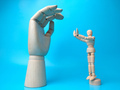 A wooden mannequin makes a pose holding a wooden hand on a blue background - PhotoDune Item for Sale