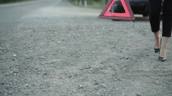 Unrecognizable Woman with Broken Automobile Installing Red Triangle Sign on Road