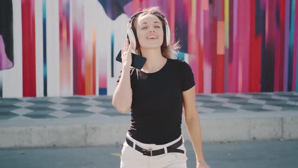 Portrait of an Attractive Girl Carefree Dancing Outdoors. Young Woman in Headphones and with a Paper