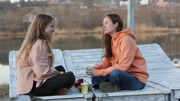 Two Teenage Girl Sitting In The Wooden Deck Chairs On The Lake Shore 4