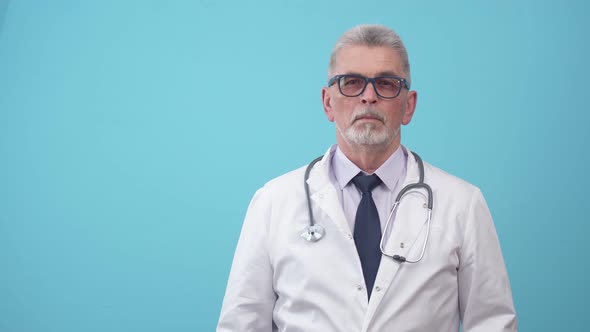 Adult Doctor in Medical Gown with a Stethoscope Thinks and Leans Hand Against Chin in the Studio a