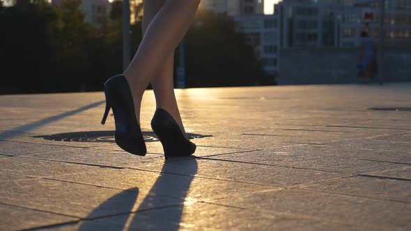 Follow To Female Legs in High Heels Shoes Walking Along City Street in Sunset Time