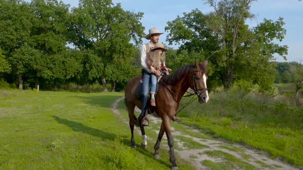 Cowboy and His Daughter on Horseback on a Forest Lawn