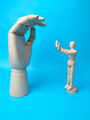 A wooden mannequin makes a stunt holding a wooden hand on a blue background - PhotoDune Item for Sale