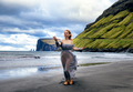 A  red-haired woman dressed as an elf stays on the beach with black sand. Faroe Islands, Denmark - PhotoDune Item for Sale