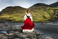 A  redhead girl stays on stone near ocean coastline in old-fashioned clothes. Faroe Islands, Denmark - PhotoDune Item for Sale