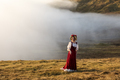 A  woman in old-fashioned clothes stays on the grass field in the highland. Faroe Islands, Denmark - PhotoDune Item for Sale