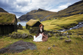A young woman sits near a stone fence in old-fashioned clothes. Saksun,  Streymoy, Faroe Islands - PhotoDune Item for Sale