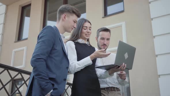 Portrait Young Woman and Two Men in Formal Wear Discussing Project on the Laptop on the Terrace