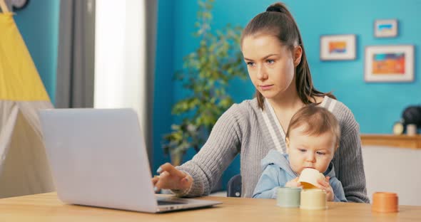 Young Attractive Girl Focused Sits at Desk and Works on Computer Searches for Deals Writes