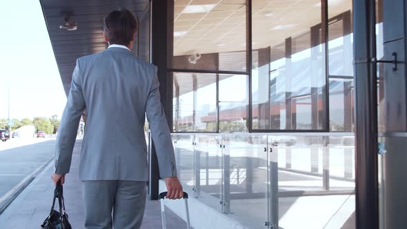 Elegant businessman walking with suitcase along the airport. Young mail entrepreneur.