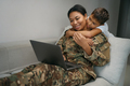 Military mom is comfortably seated with laptop at home on couch - PhotoDune Item for Sale
