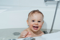 A small smiling beautiful baby bathes in a white bath. Cheerful photography. - PhotoDune Item for Sale