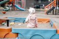 A small child alone sits in a sandbox on the playground in the yard - PhotoDune Item for Sale