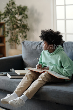 Pensive African American schoolboy with open encyclopaedia and pencil over page